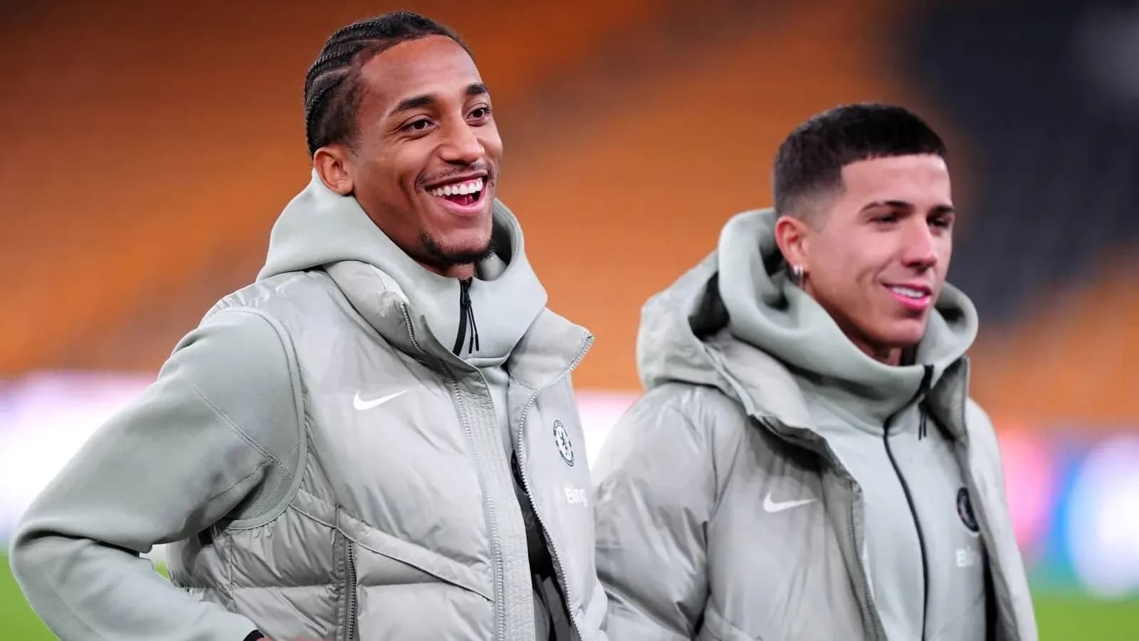 Two players smiling in training jackets on pitch