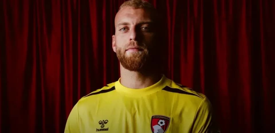 Goalkeeper in yellow kit posing against red backdrop
