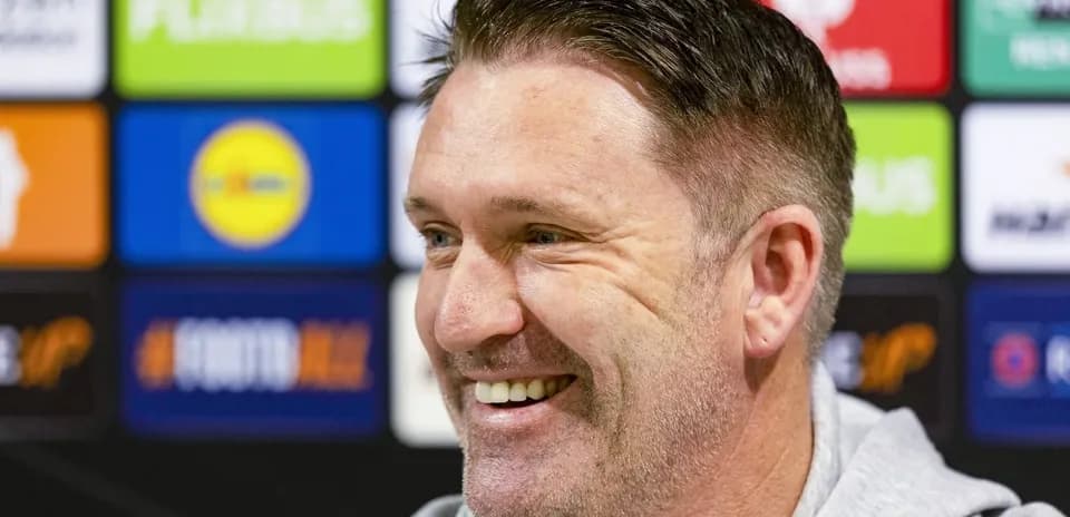 Smiling man at press conference with sponsor backdrop