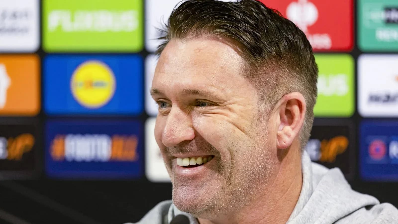Smiling man at press conference with sponsor backdrop