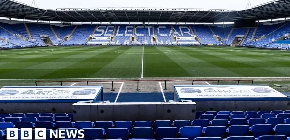 Empty football stadium with blue seats and green pitch