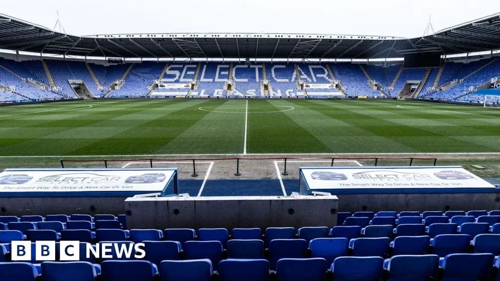 Empty football stadium with blue seats and green pitch