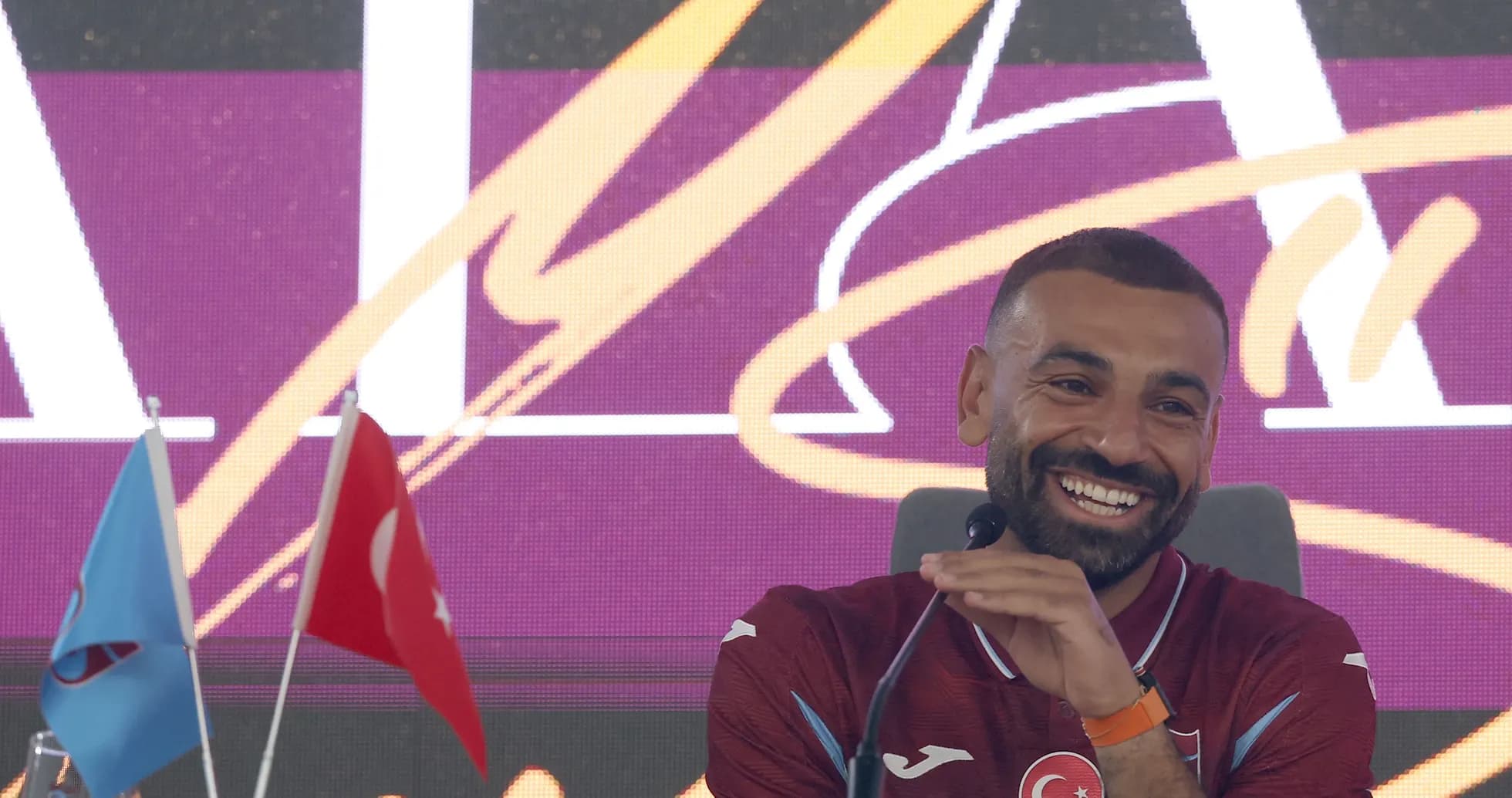 Player smiling during press conference with flags