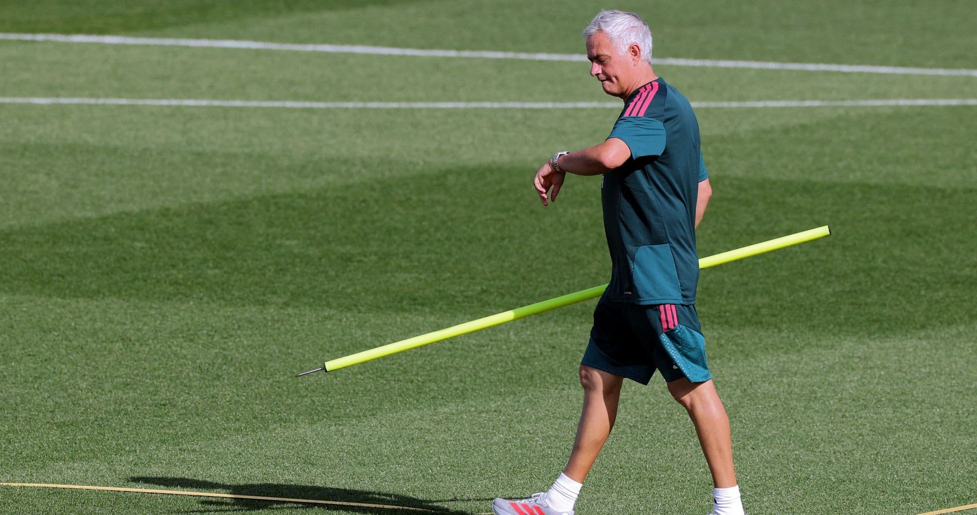 Coach walking on training pitch with training pole