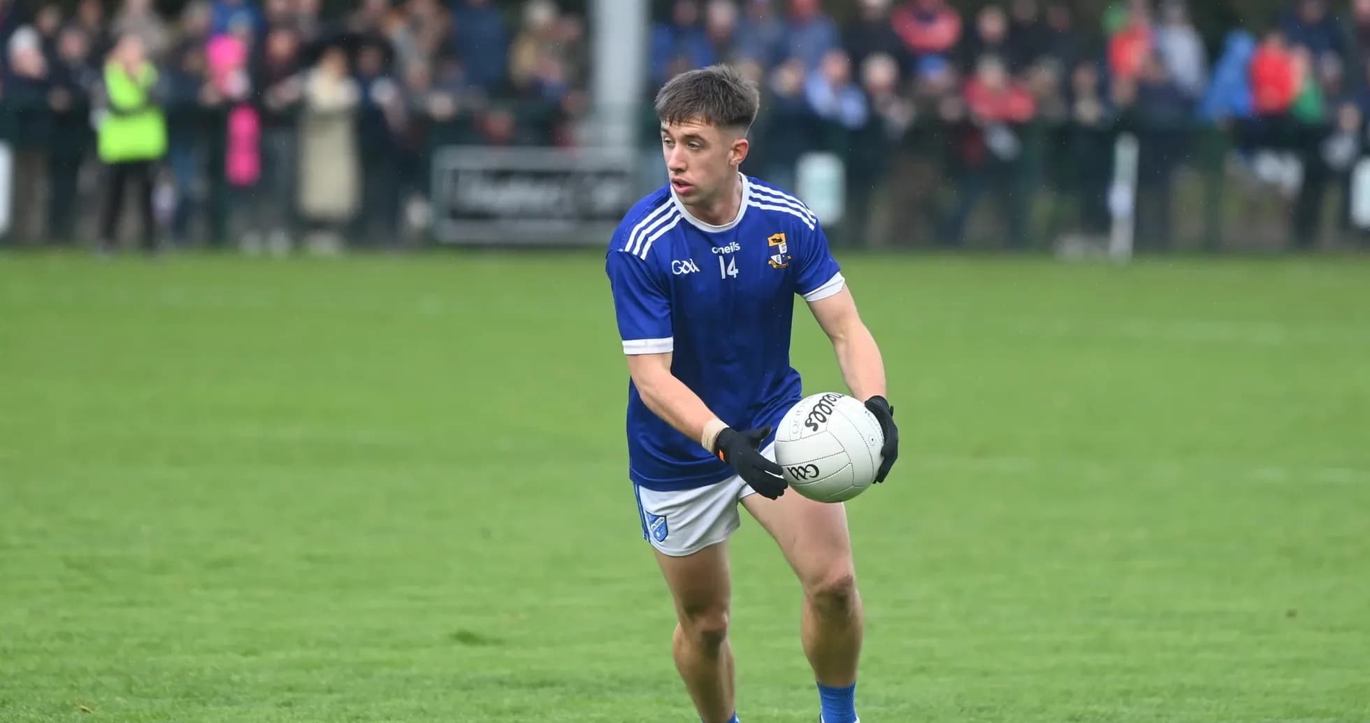 Player in blue jersey holding Gaelic football on pitch