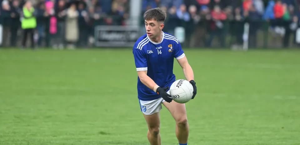 Player in blue jersey holding Gaelic football on pitch