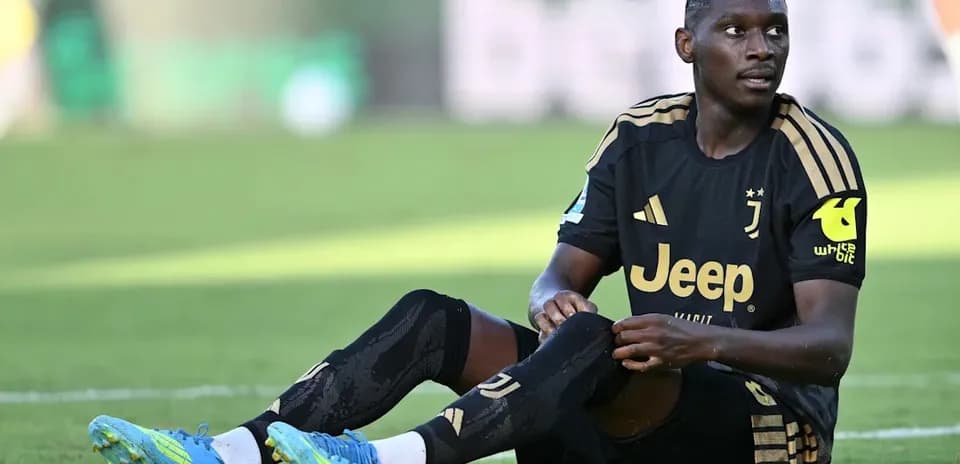 Player sitting on field during match, wearing Juventus kit