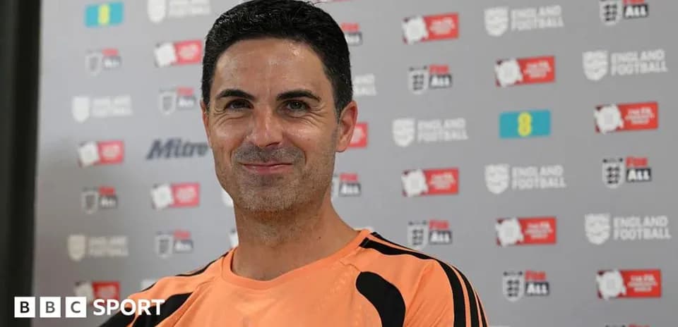 Coach smiling during press conference with branding backdrop