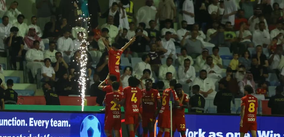 Players celebrating a goal with fireworks in background