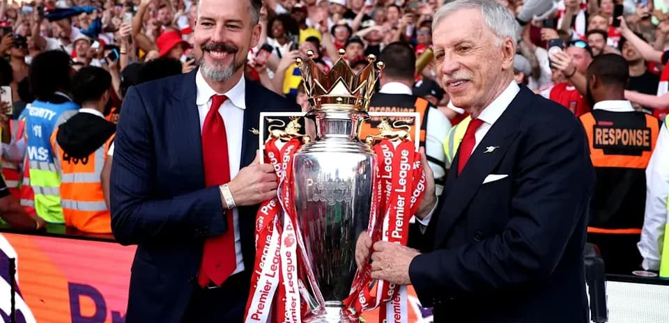 Two men holding Premier League trophy with fans celebrating