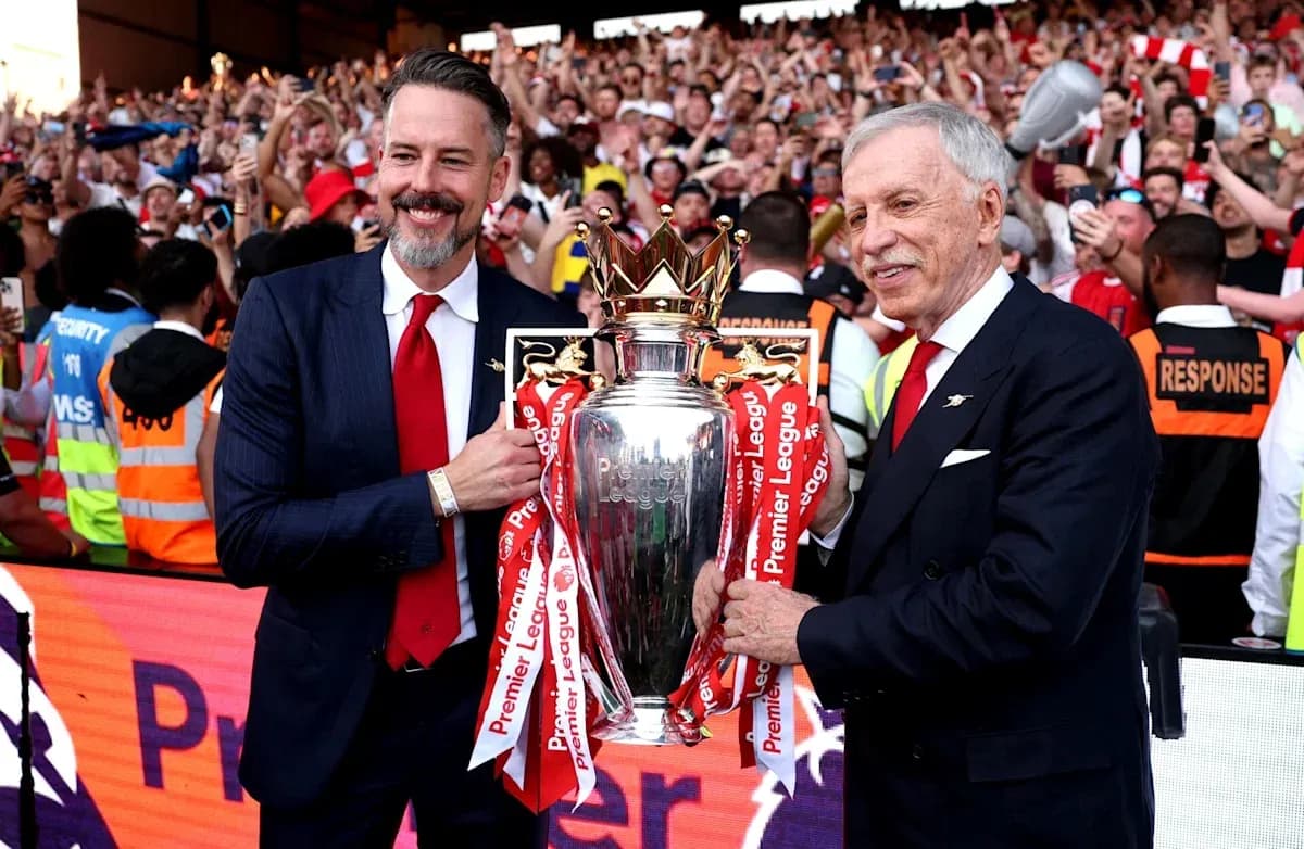Two men holding Premier League trophy with fans celebrating