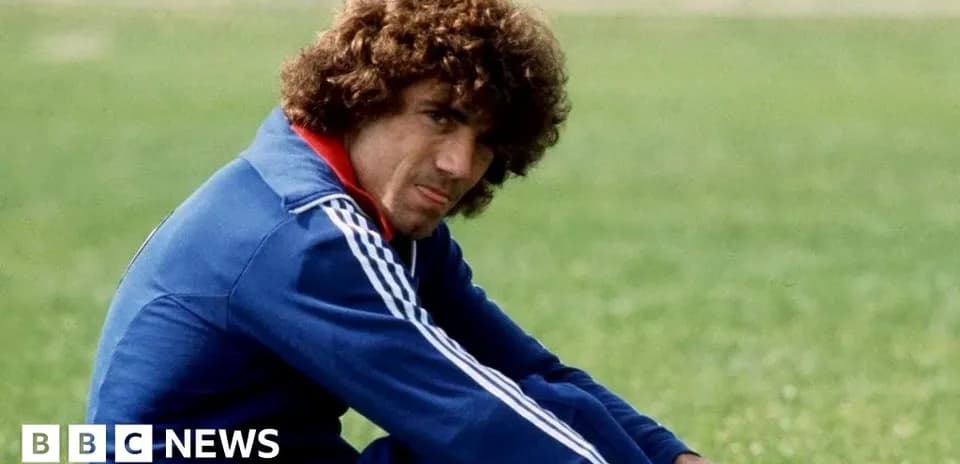 Football player sitting on grass field in tracksuit
