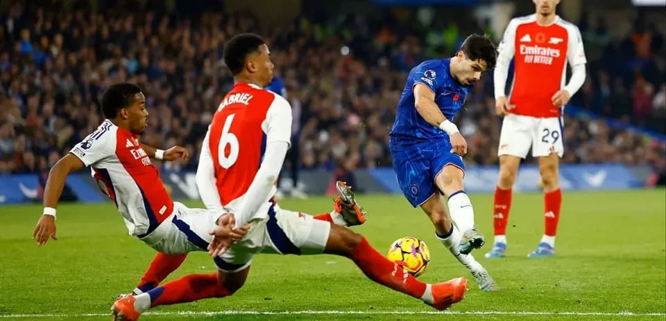 Chelsea player shooting while Arsenal defenders attempt to block