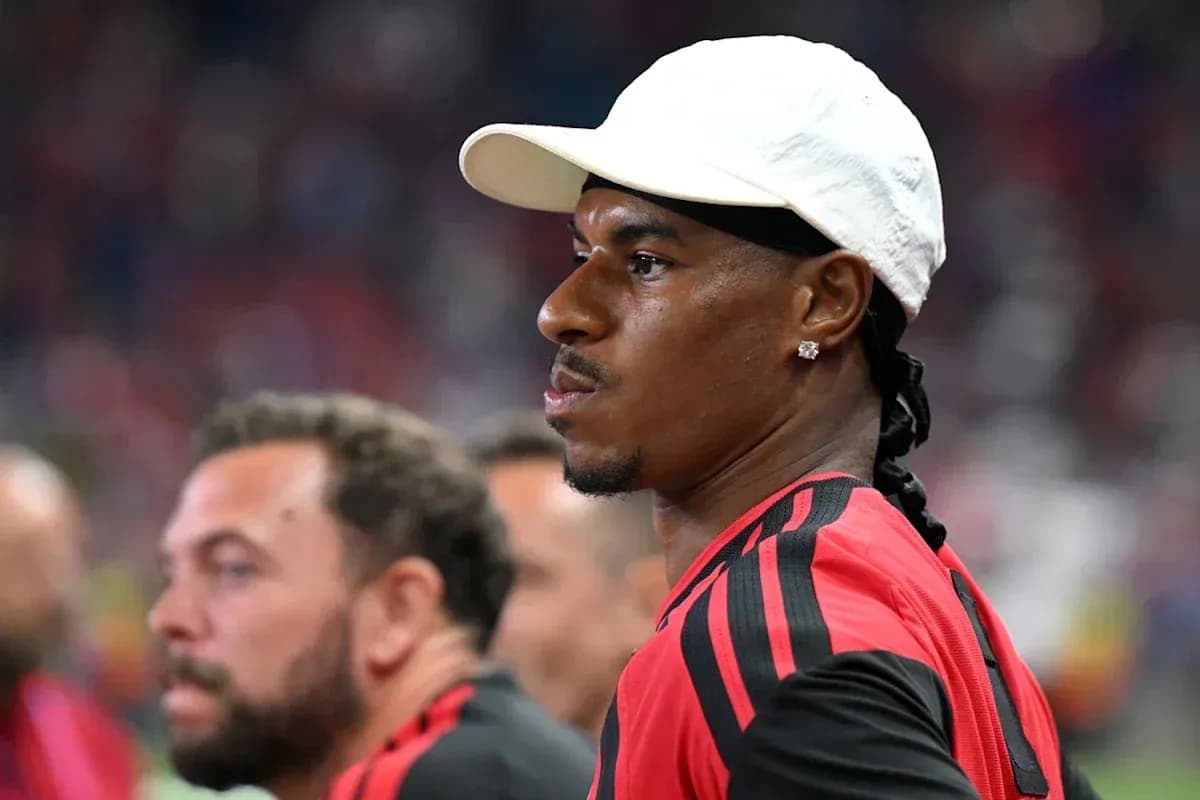 Player in red jersey observing the match sidelines