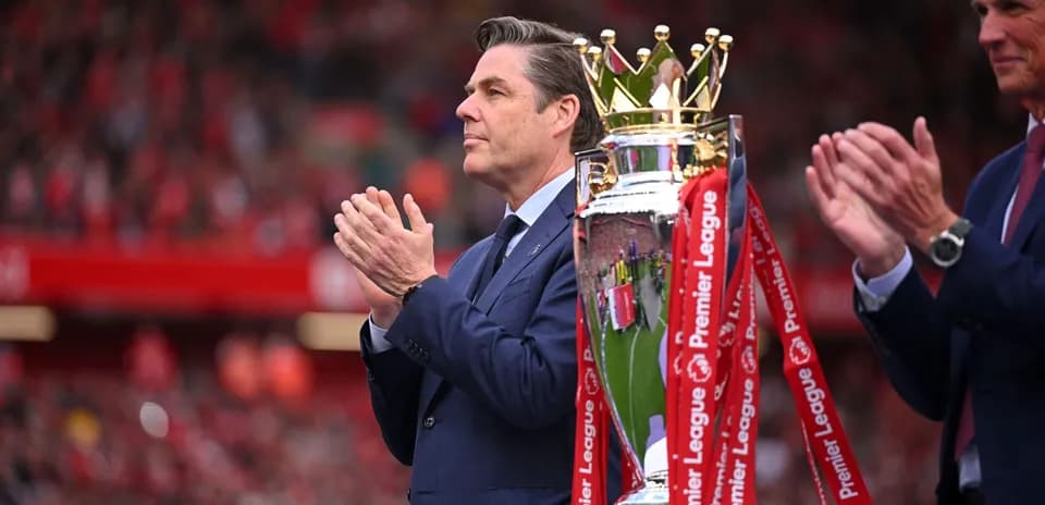 Man applauding next to Premier League trophy