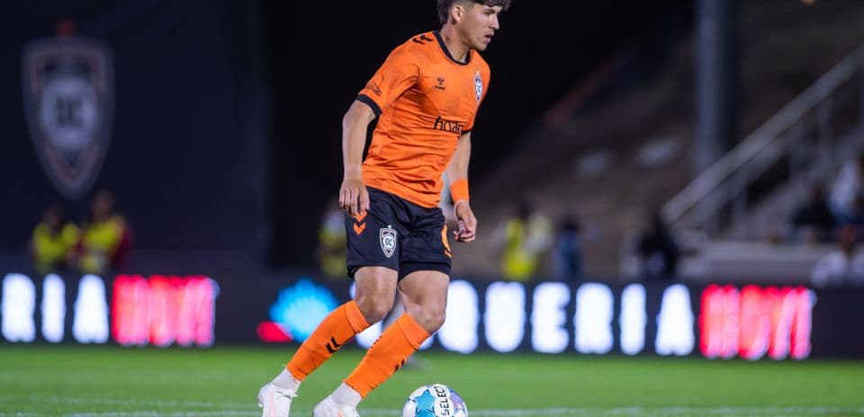 Player in orange kit dribbling ball on field