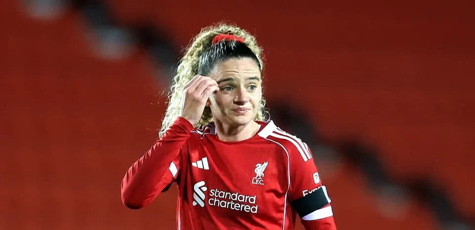 Player in red Liverpool kit adjusting hair on pitch