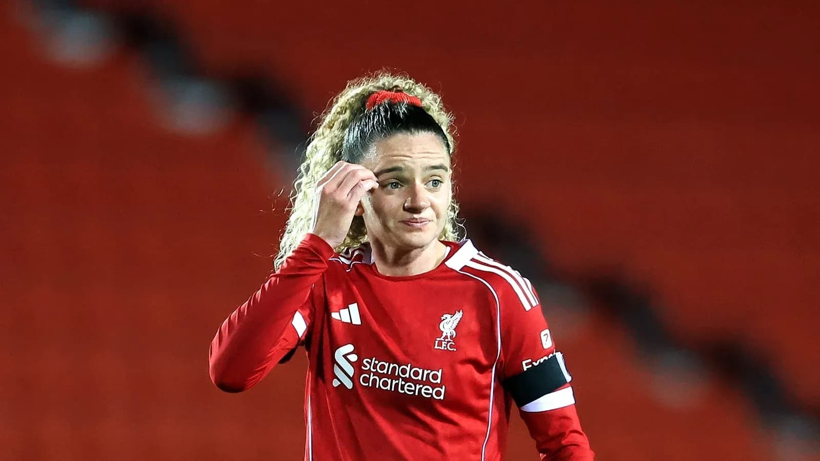 Player in red Liverpool kit adjusting hair on pitch
