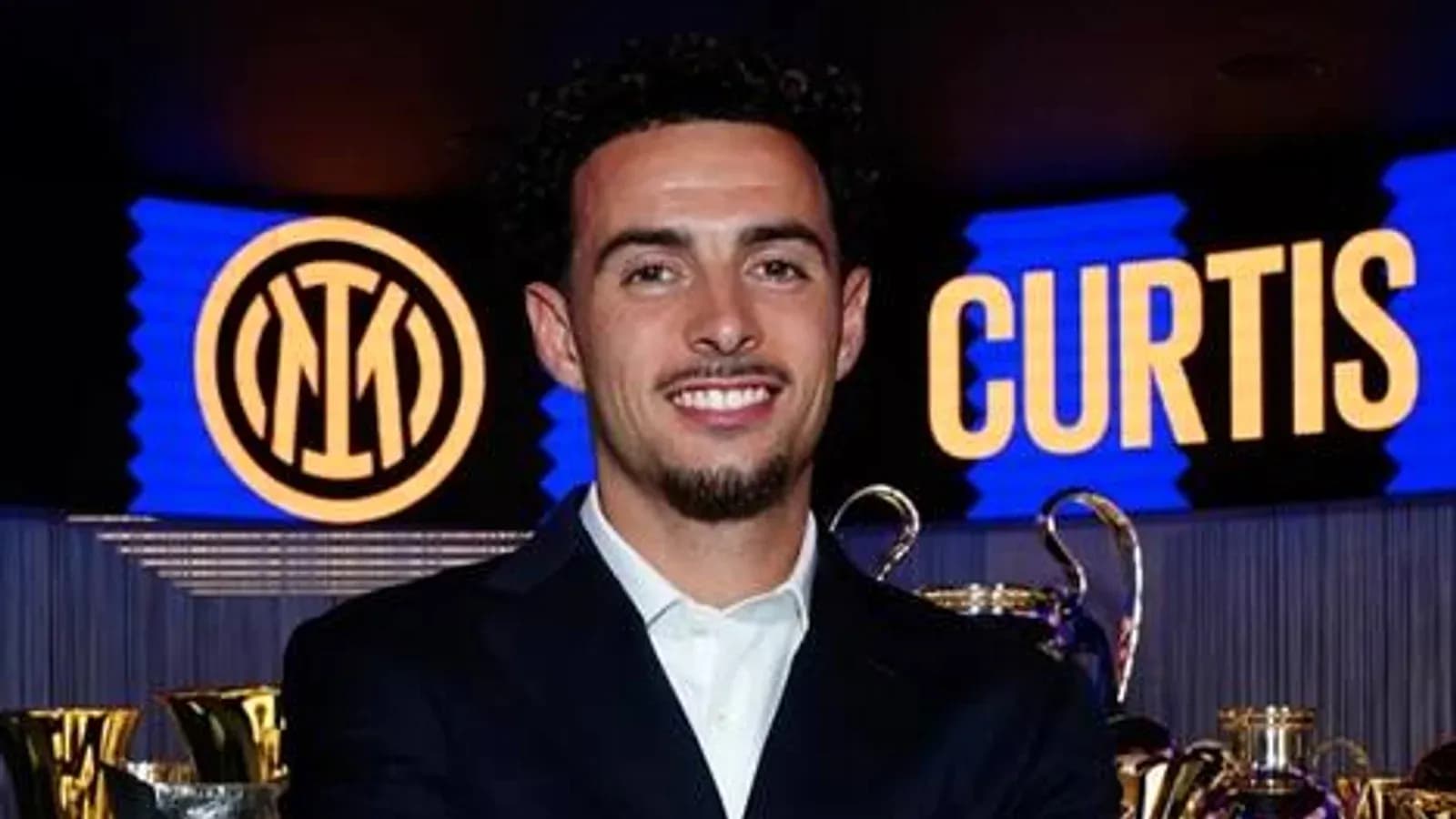 Player smiling in front of trophies and logo