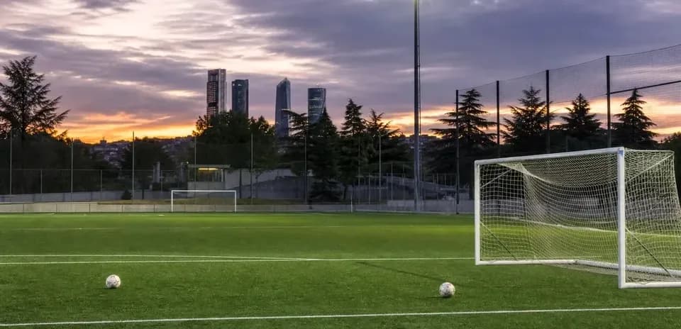 Soccer field with goalposts and city skyline at sunset