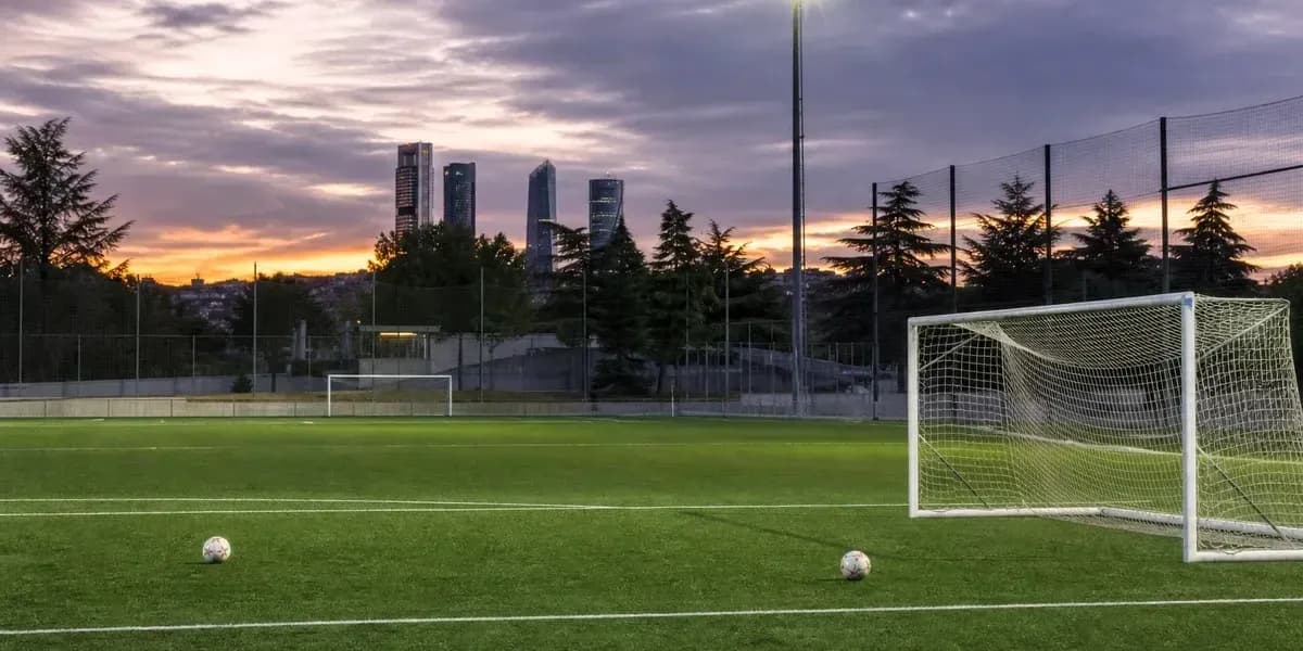 Soccer field with goalposts and city skyline at sunset