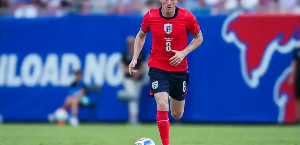 Player in red kit dribbling soccer ball on field