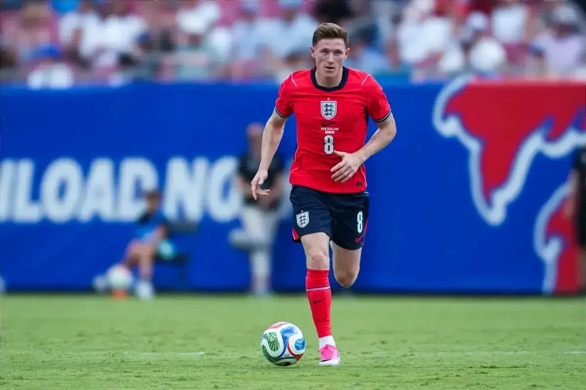 Player in red kit dribbling soccer ball on field