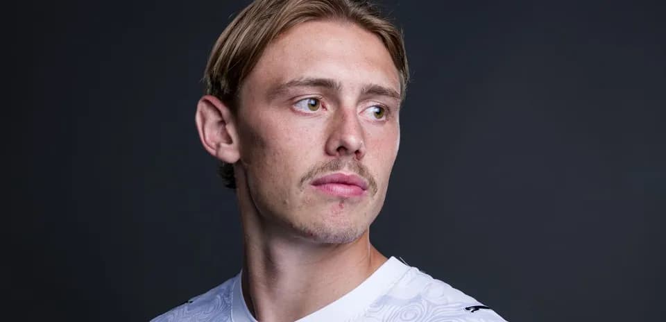 Football player posing in white jersey against dark background