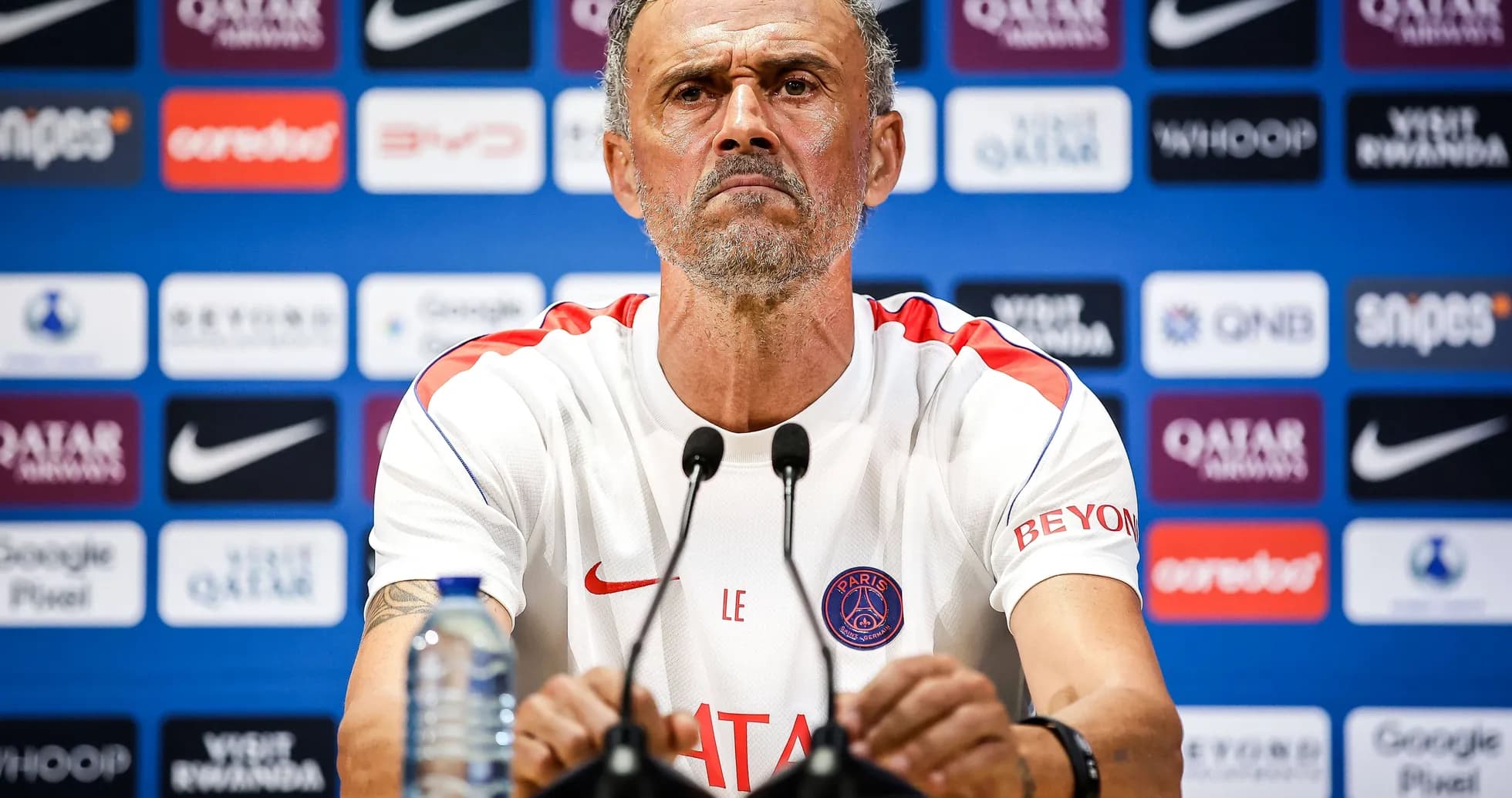 Manager at press conference with sponsor logos in background