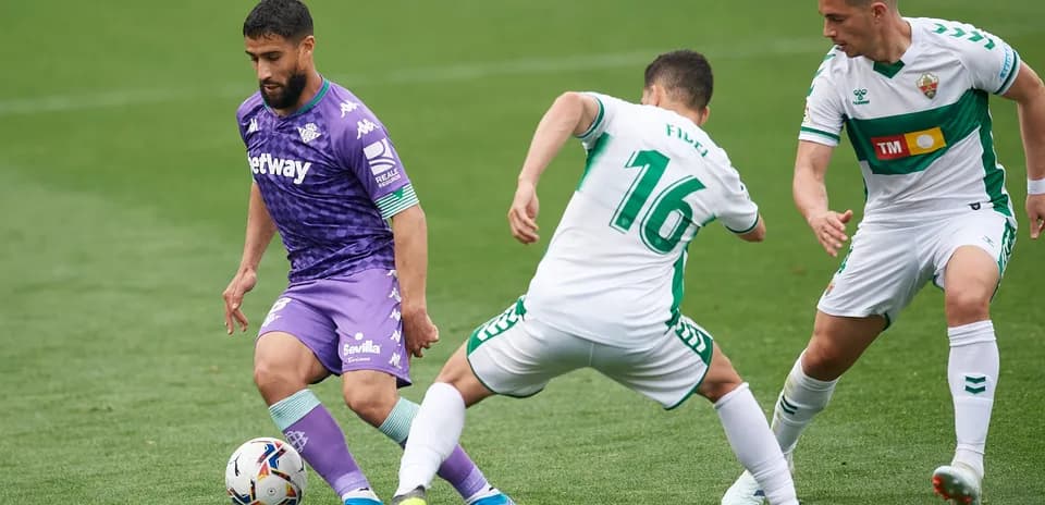Real Betis player dribbling past Elche defenders