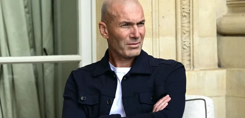 Man seated outdoors with arms crossed, looking thoughtful