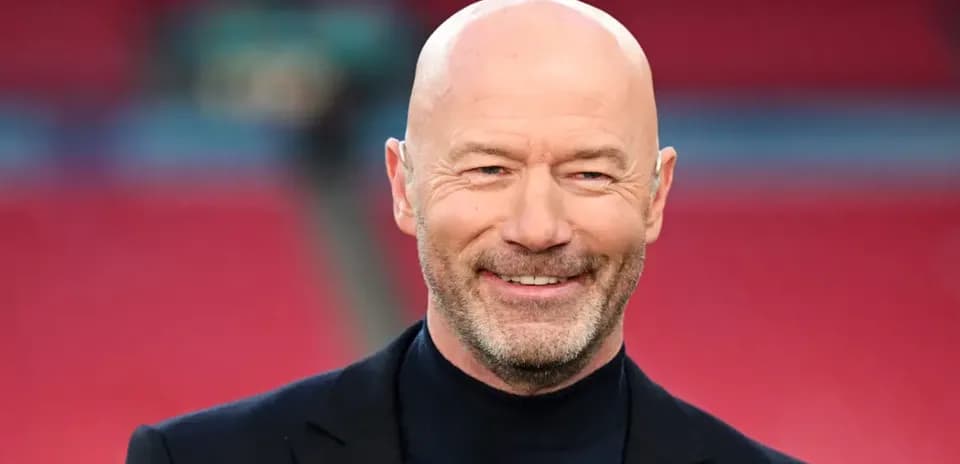 Bald man in a black suit smiling at stadium