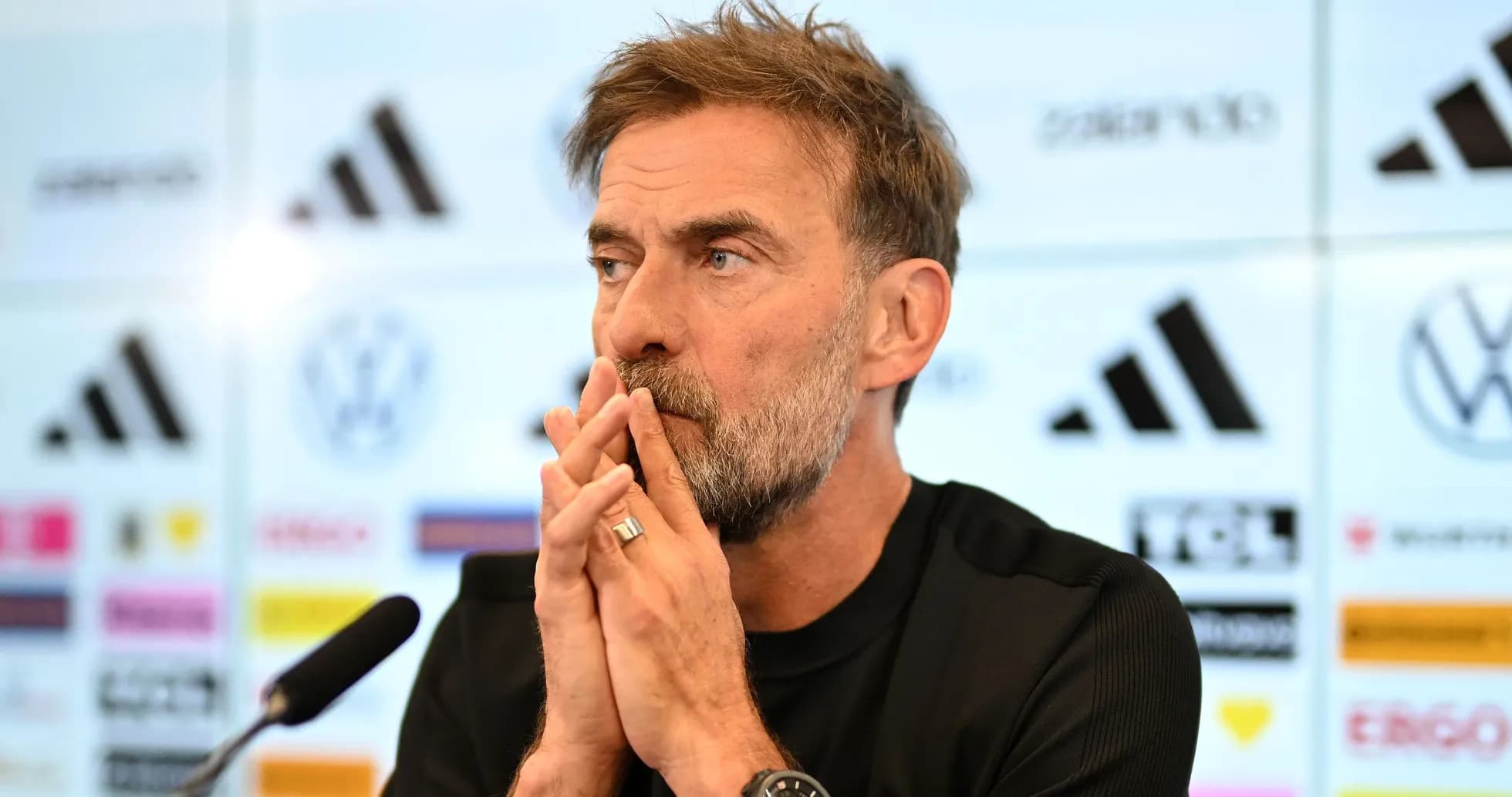 Manager speaking at press conference with logos in background