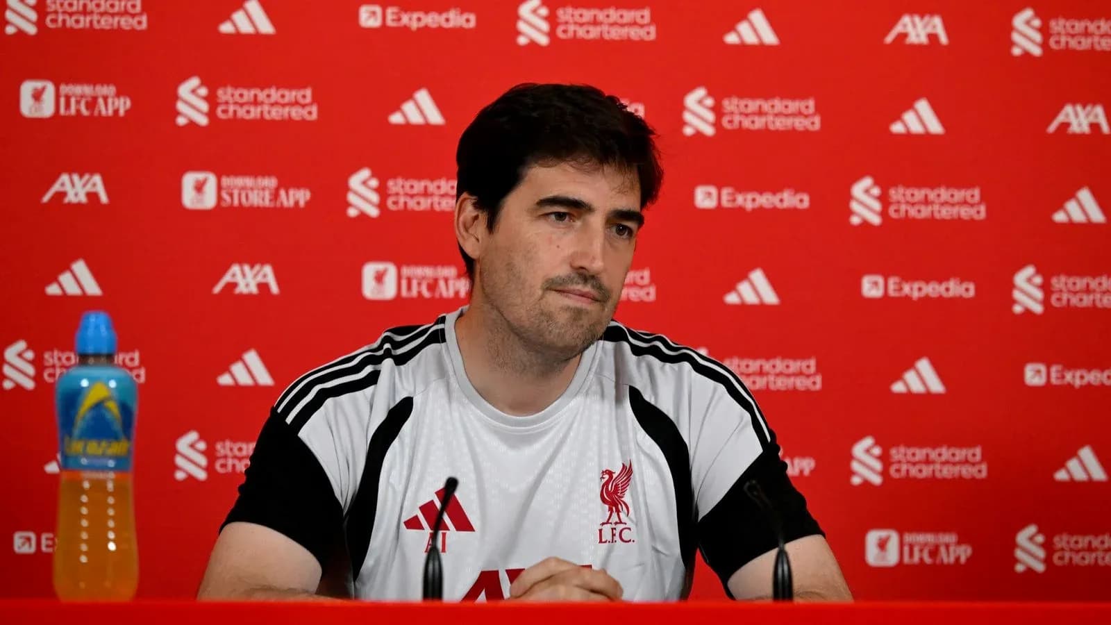 Man at press conference with Liverpool branding backdrop