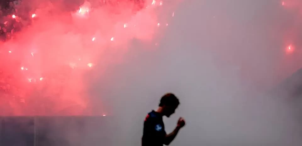 Player celebrating amidst smoke and flares in stadium