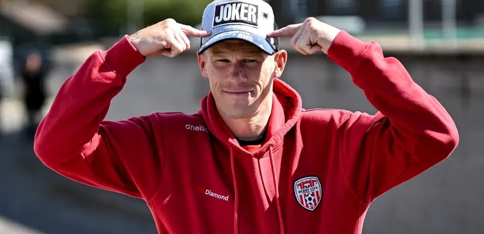 Person in red hoodie pointing at 'JOKER' cap