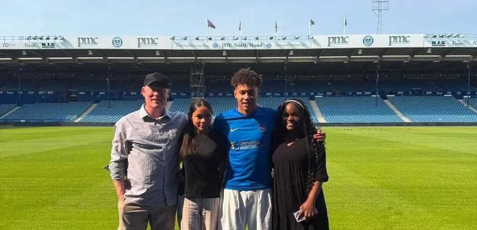 Four individuals posing on football pitch at stadium