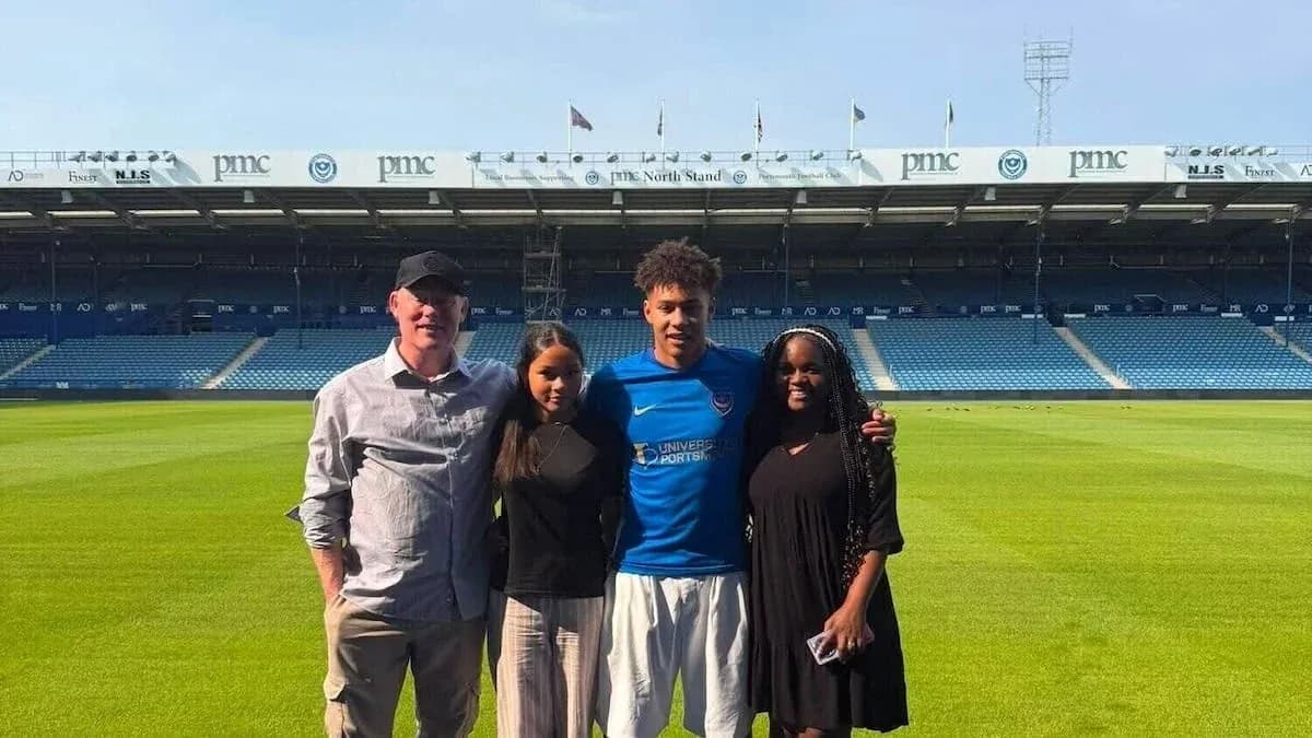 Four individuals posing on football pitch at stadium