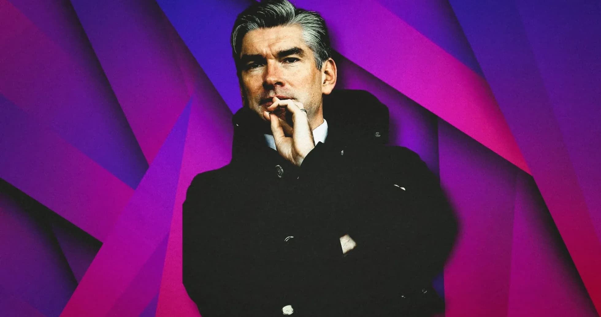 Man in coat with hand on chin against colorful background