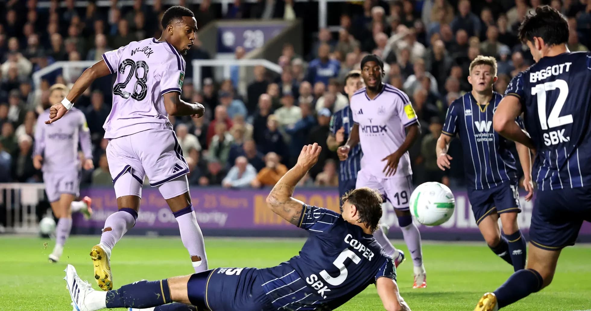 Player in purple jersey scoring against fallen defender Player in purple jersey scoring against fallen defender