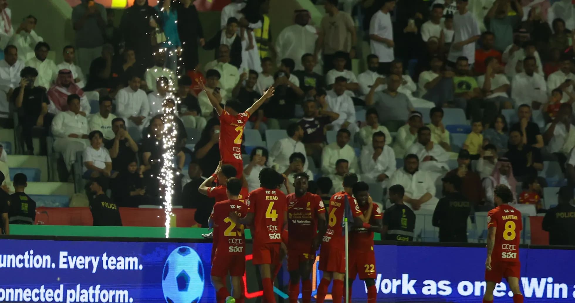 Players celebrating a goal with fireworks in background Players celebrating a goal with fireworks in background