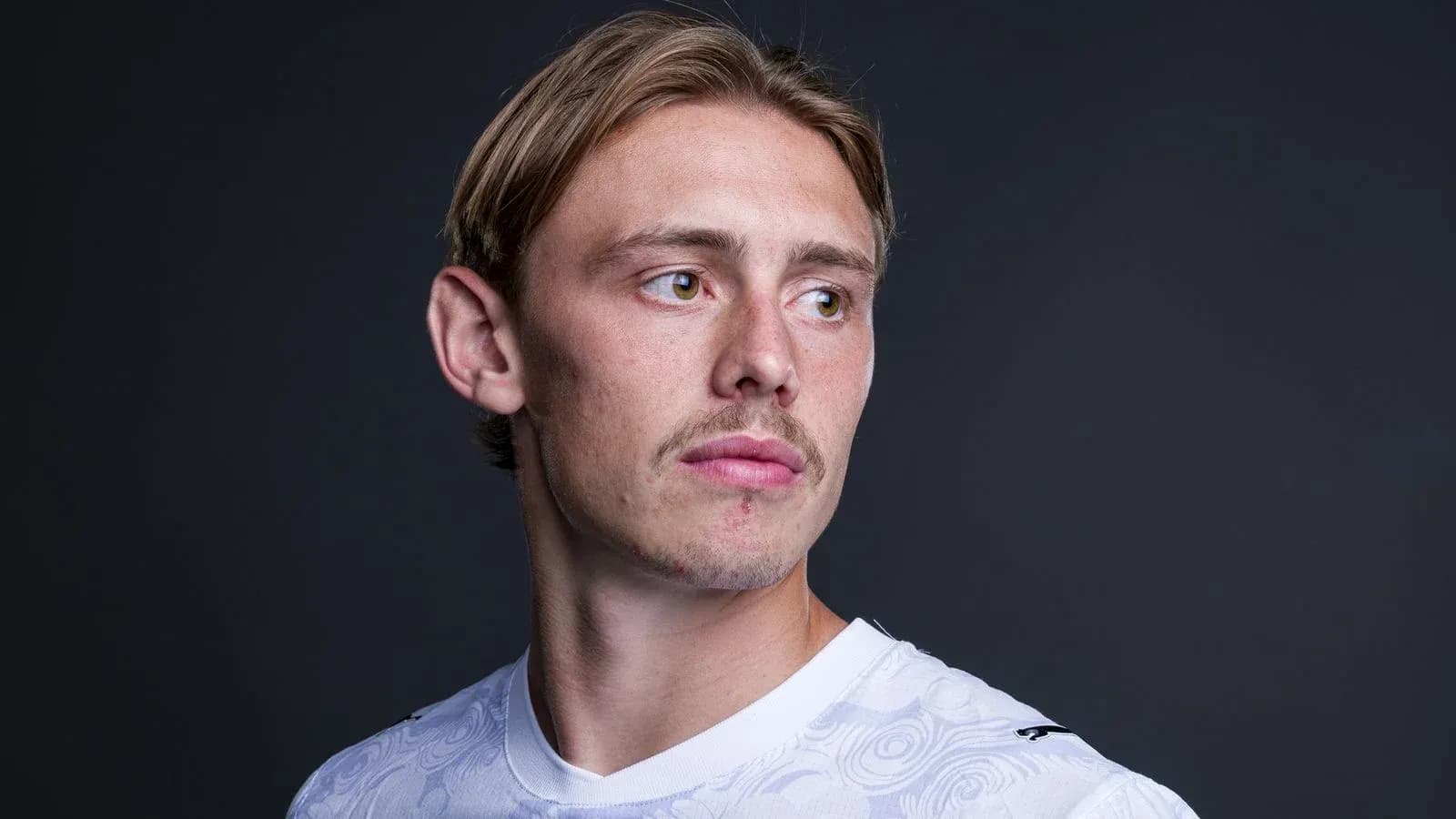 Football player posing in white jersey against dark background Football player posing in white jersey against dark background